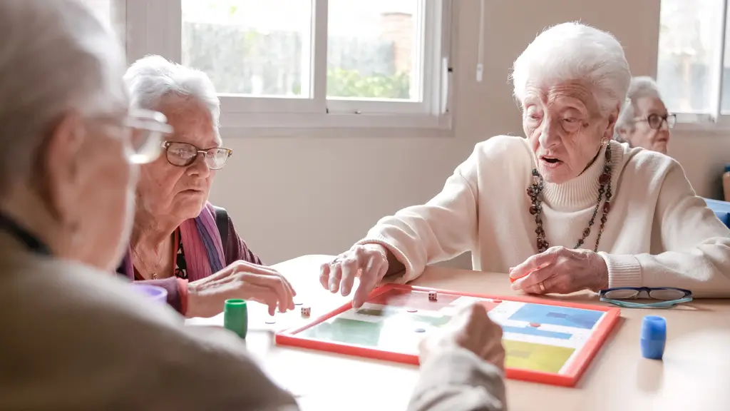 Mehrere ältere Menschen sitzen an einem Tisch und spielen gemeinsam ein Brettspiel mit Würfeln und Spielfiguren
