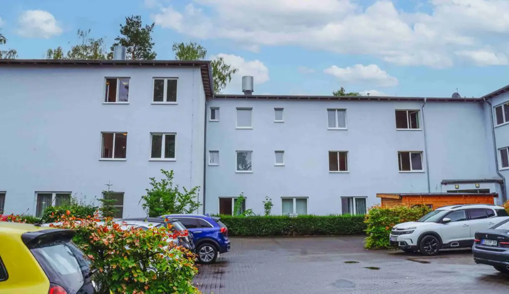 Mehrstöckiges Wohngebäude mit mehreren Fenstern und parkenden Autos davor